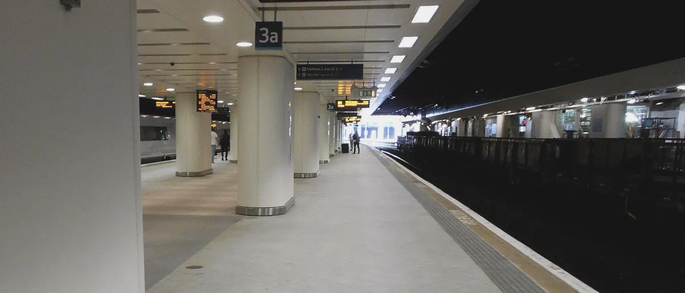 A pale platform runs past white columns towards daylight, its edge marked in yellow beside the track.