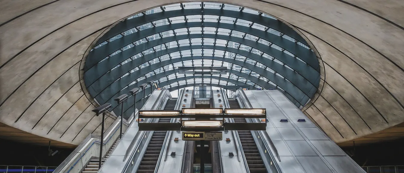 Banks of escalators rise side by side beneath a vast glass canopy set into a curved concrete shell.
