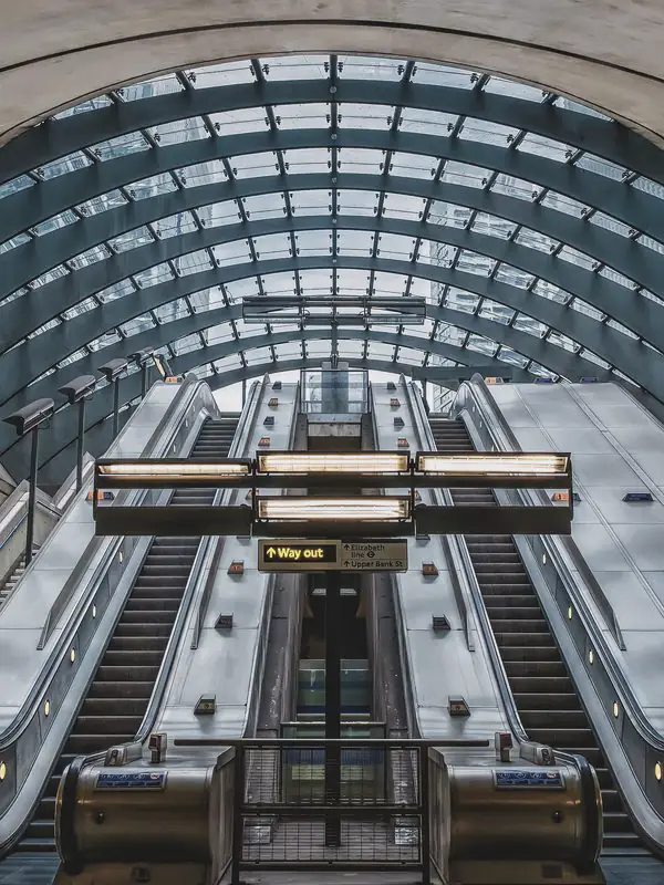 Banks of escalators rise side by side beneath a vast glass canopy set into a curved concrete shell.