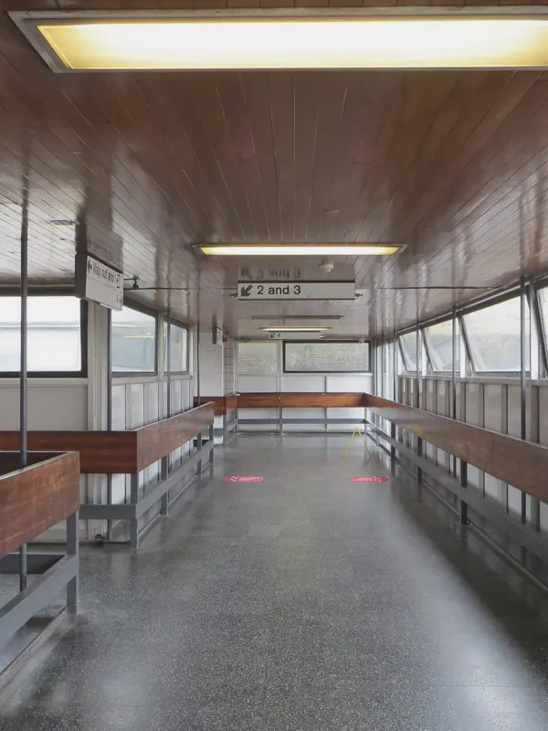 An empty footbridge with a timber ceiling and long benches runs straight ahead between windows.