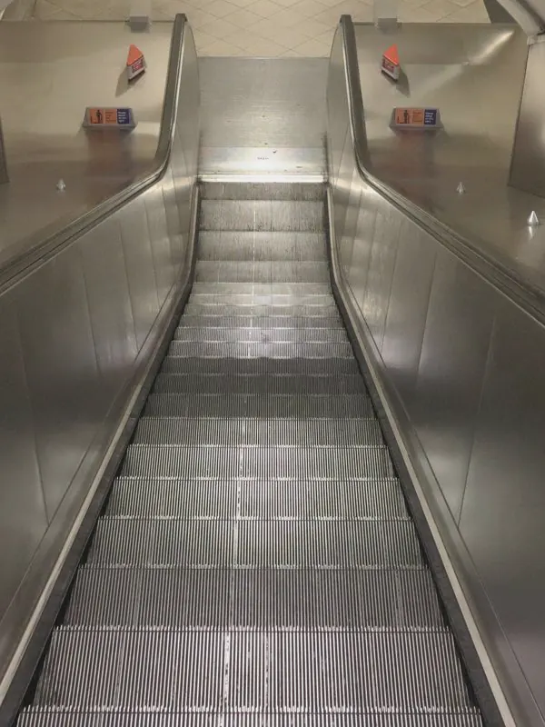 A steel escalator runs between brushed metal walls to a tiled, lit landing under a curved ceiling.