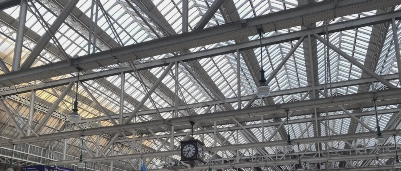 A glazed lattice roof spans the station concourse, its old clock hanging beneath the steel beams.