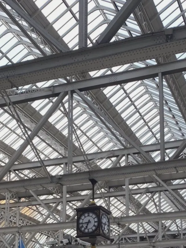 A glazed lattice roof spans the station concourse, its old clock hanging beneath the steel beams.