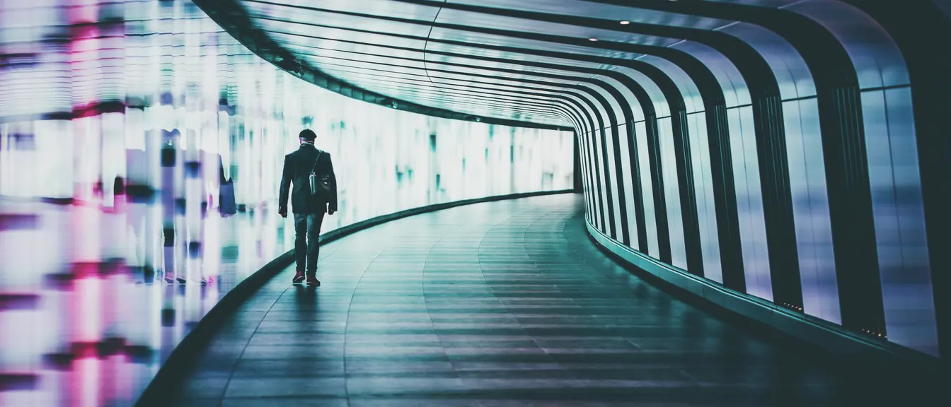 A curving tunnel lined with a glowing light wall, its floor sweeping round to a bright far end.