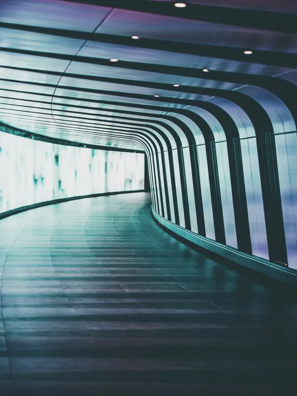 A curving tunnel lined with a glowing light wall, its floor sweeping round to a bright far end.