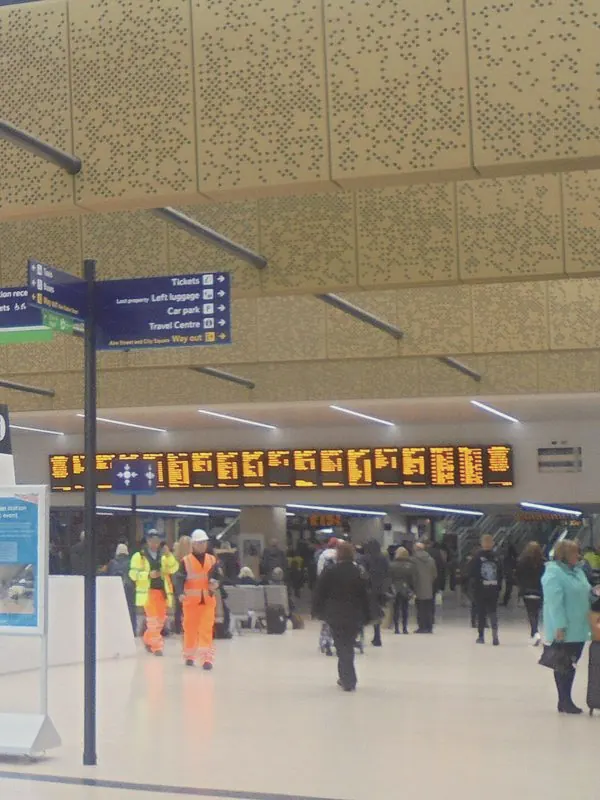 A gold perforated ceiling and skylights hang over the station concourse, with travellers small below.