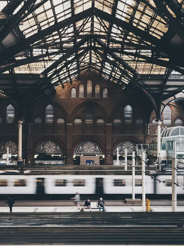 Iron roof arches and glazing span the platforms in front of a brick wall of arched windows.