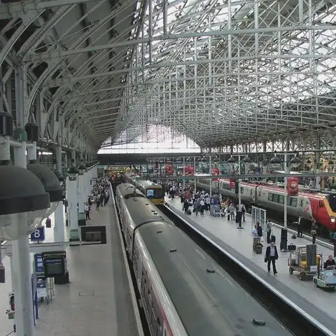 A glass and steel trainshed roof covers busy platforms and waiting trains, seen from a footbridge above.