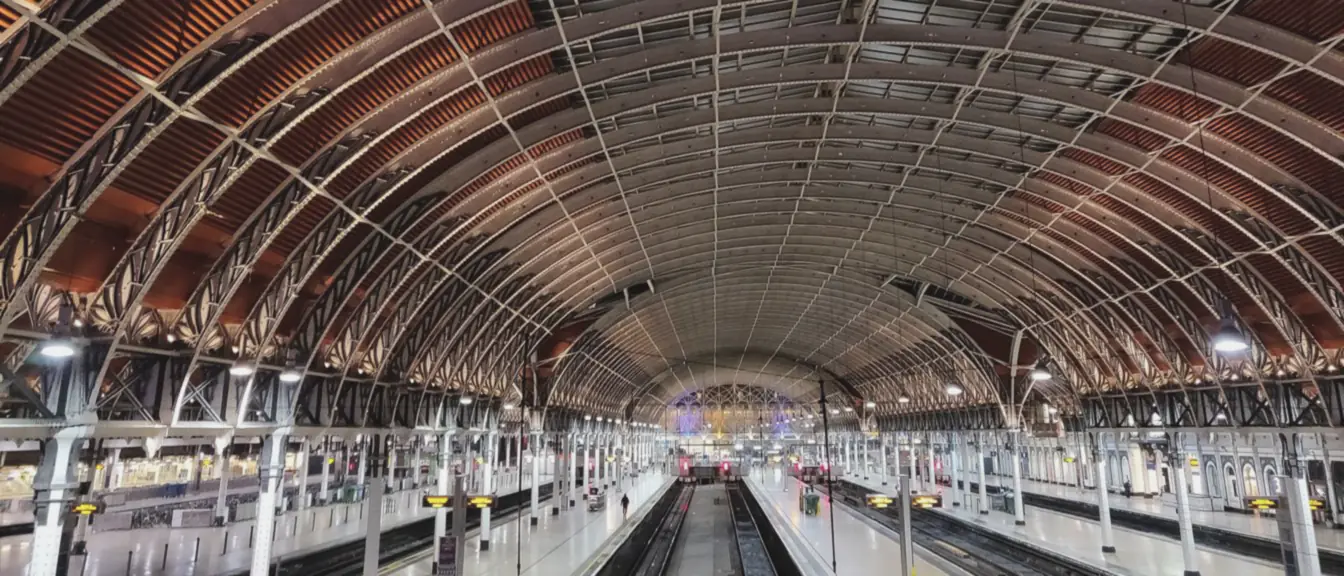 Wrought iron roof ribs arch over the platforms and tracks, converging on the lit far end of the trainshed.