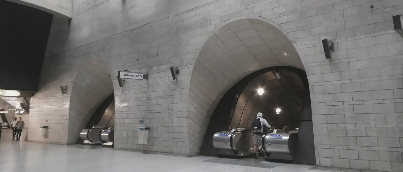 Stone arches in a tall pale hall open onto escalators, with one rider small at the foot.