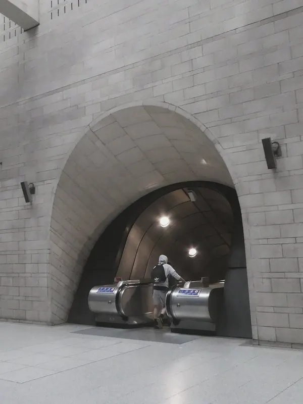 Stone arches in a tall pale hall open onto escalators, with one rider small at the foot.