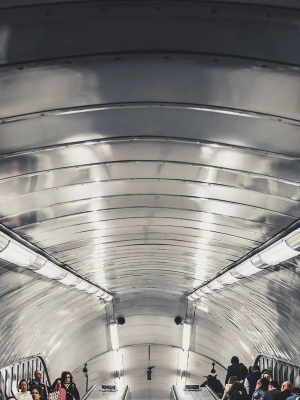 Long escalators climb beneath a ribbed tunnel ceiling and strip lights, the riders small in the distance.