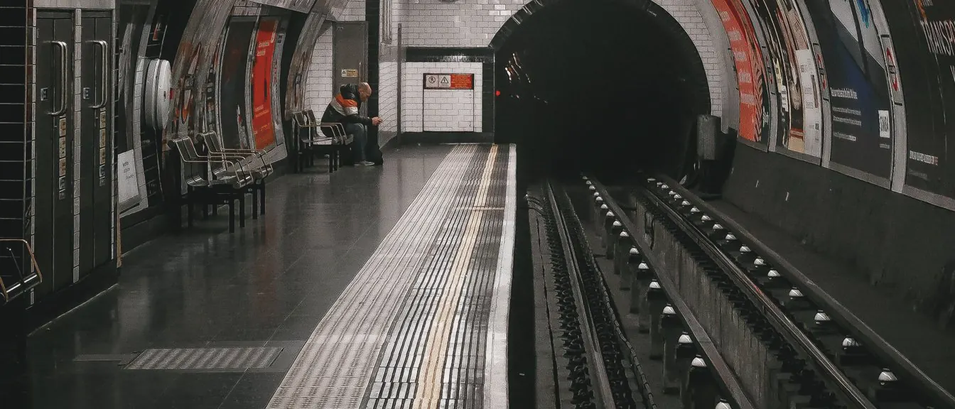 An empty Underground platform curves beside the rails into a dark tunnel mouth under a tiled ceiling.