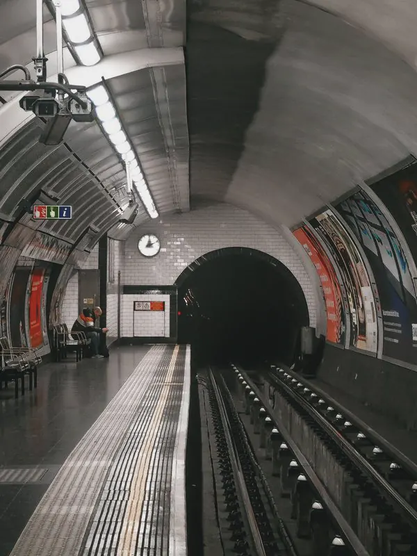An empty Underground platform curves beside the rails into a dark tunnel mouth under a tiled ceiling.